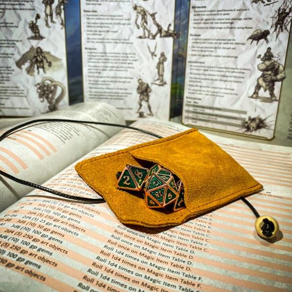 Light brown leather dice bag with green metal dice on book